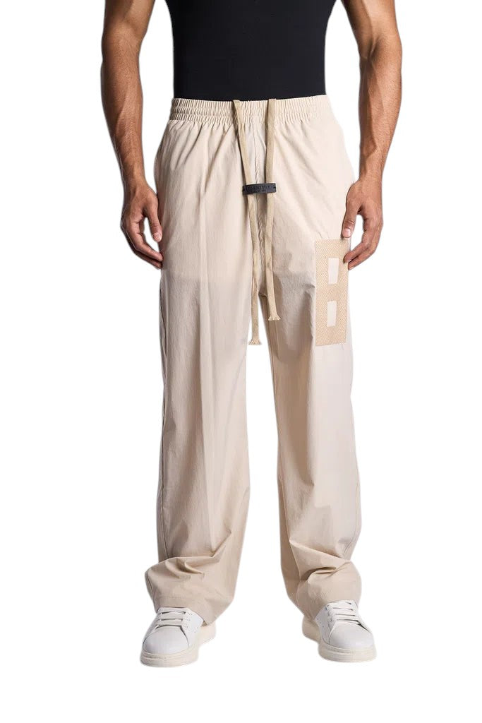 My Store ESSENTIALS beige track pants with an elastic waistband, long drawstring, and a square patch detail.