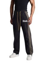 My Store Rhude black and green Aerial track pants with white logo and yellow drawstring worn by a male model